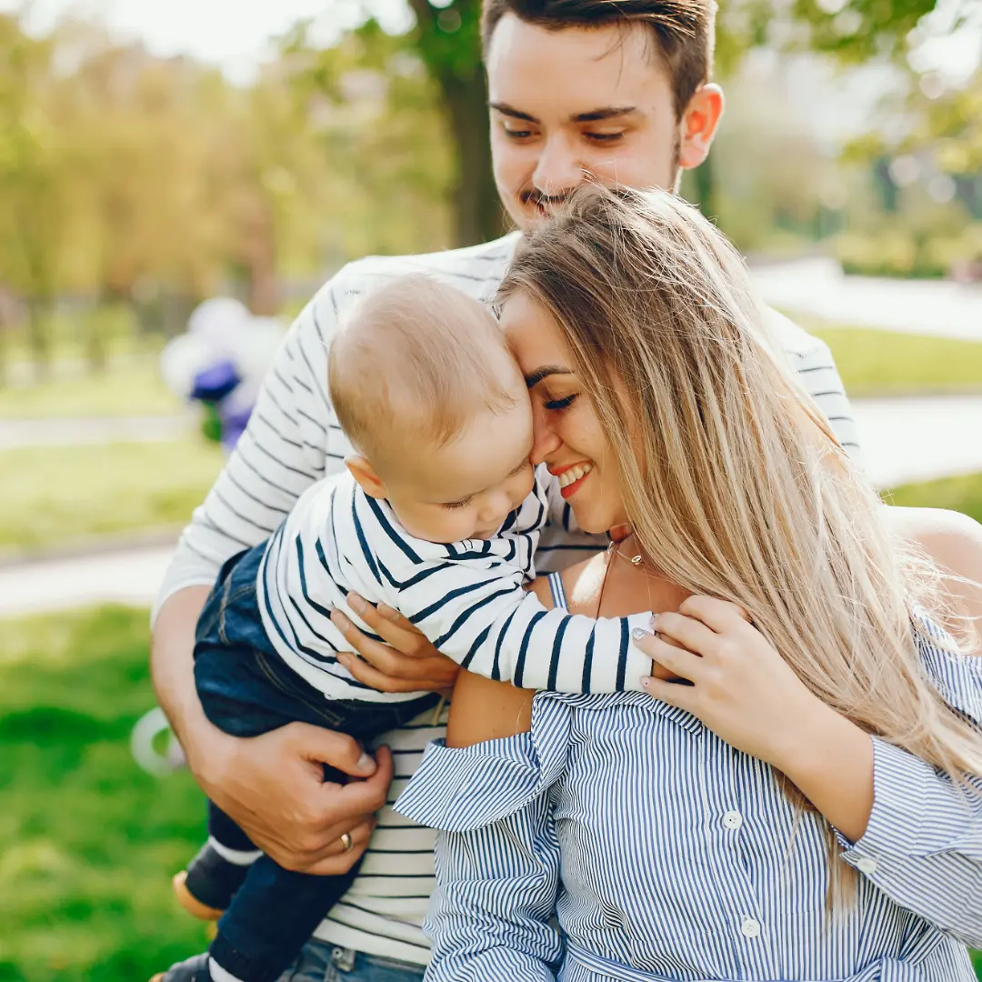 Young parents hugging their baby in a park during autumn