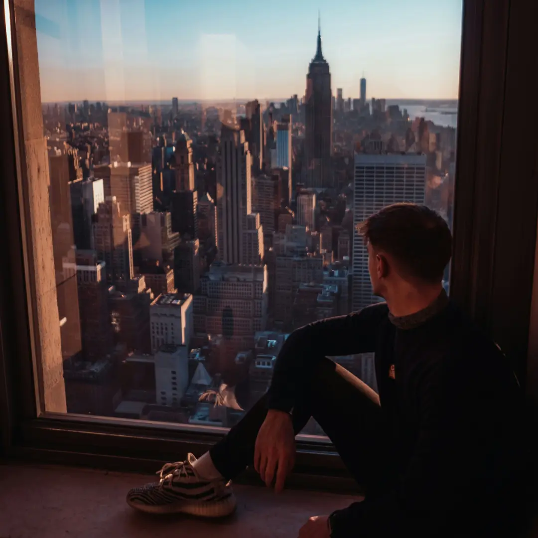 Person enjoying a panoramic view of New York City skyline from a high-rise window